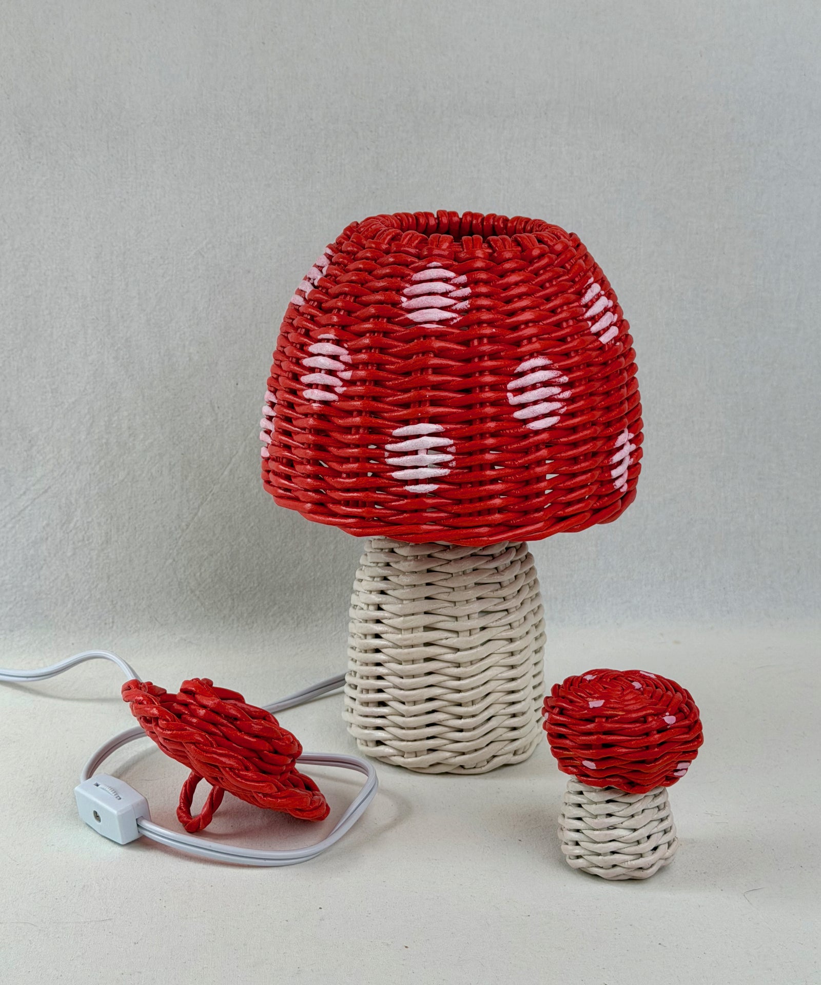 Mushroom-shaped paper vine woven lamp and a woven mushroom with red and white designs on a neutral background