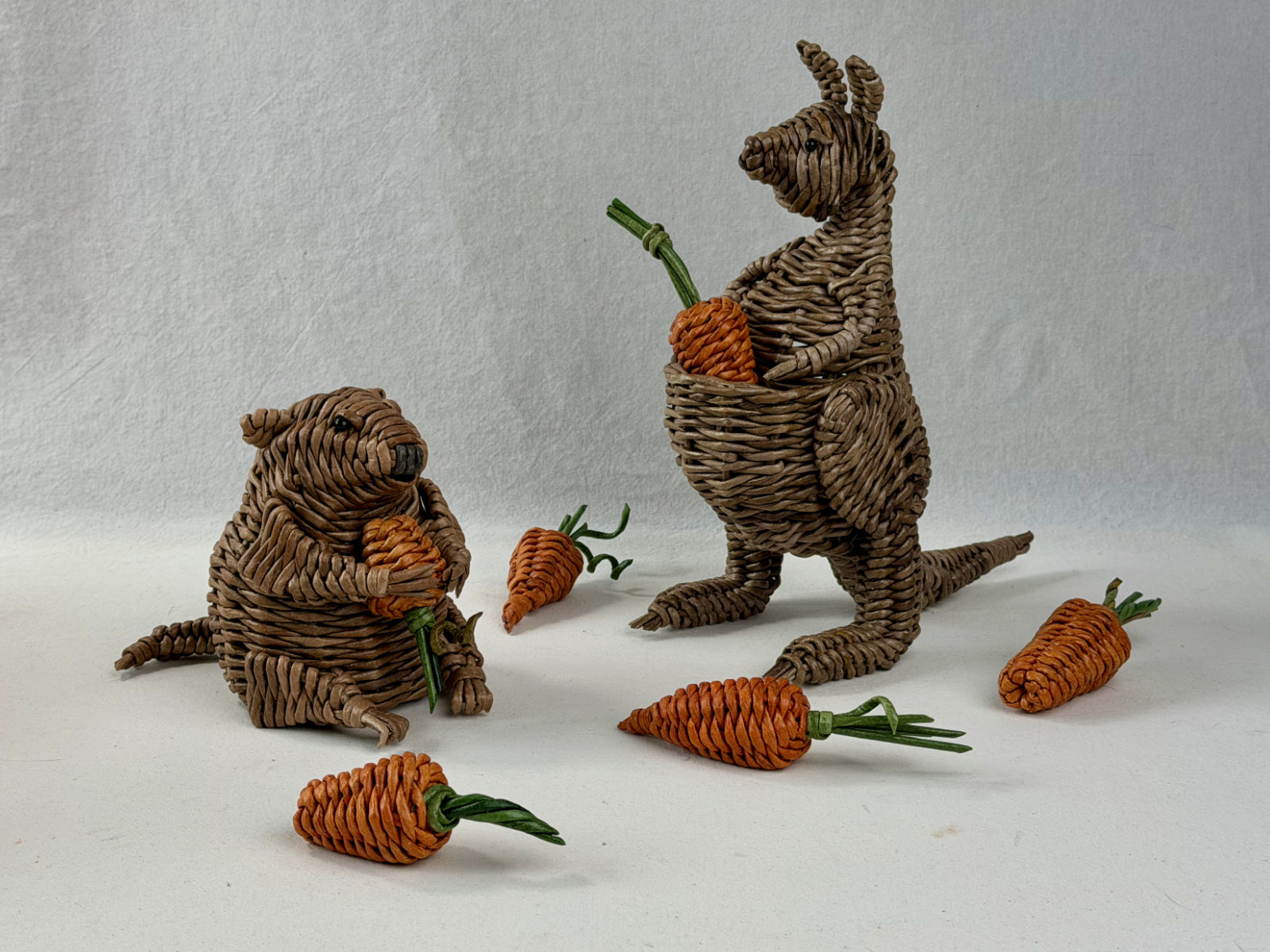 Paper vine woven groundhog and kangaroo with woven carrots on a neutral background