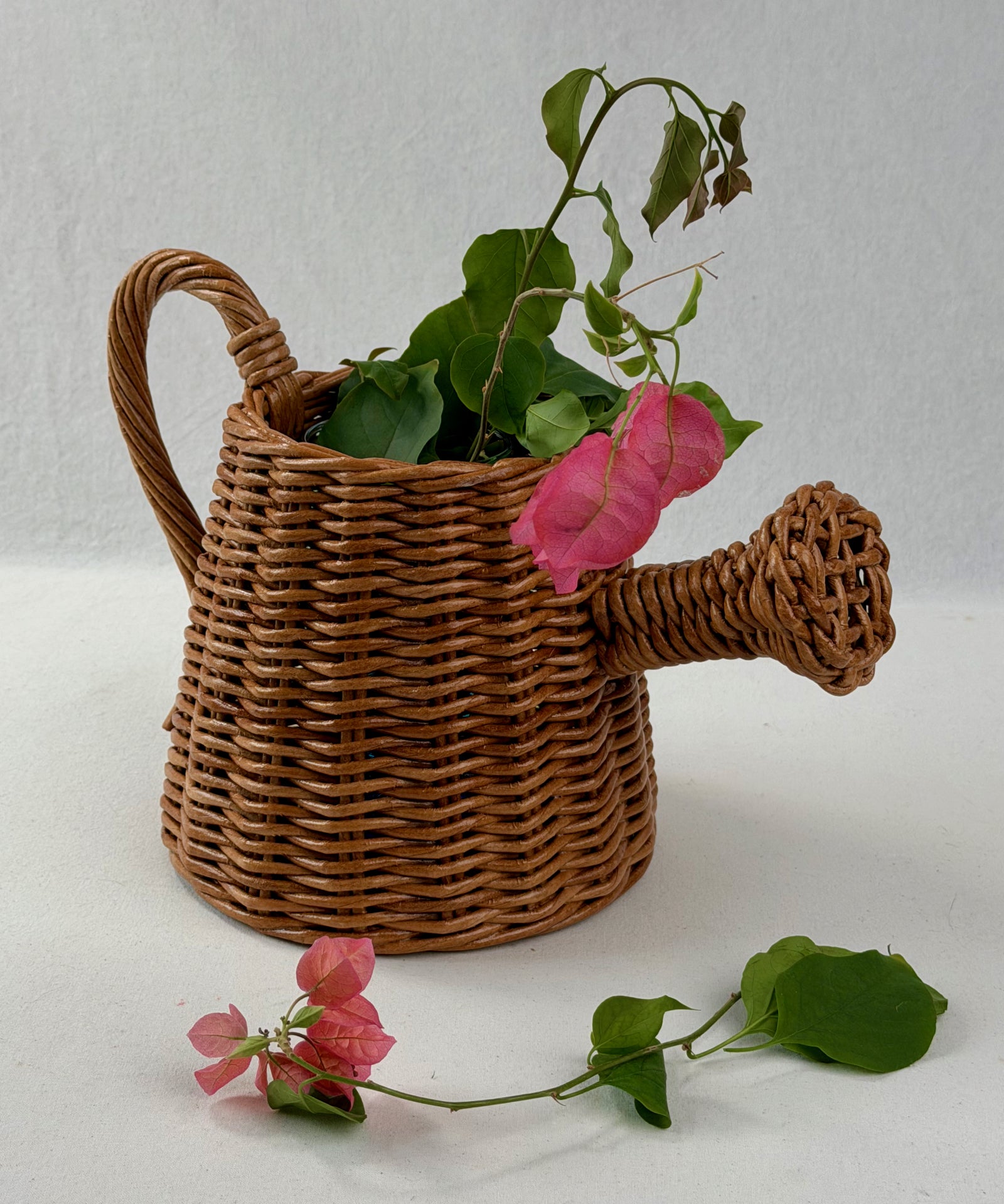 Paper vine woven watering can with pink flowers on a white background